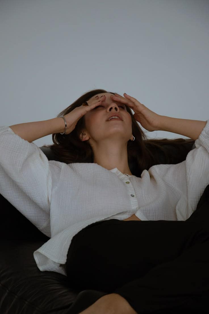Woman sitting at a desk looking stressed, hands on temples, representing anxiety and nervous system tension