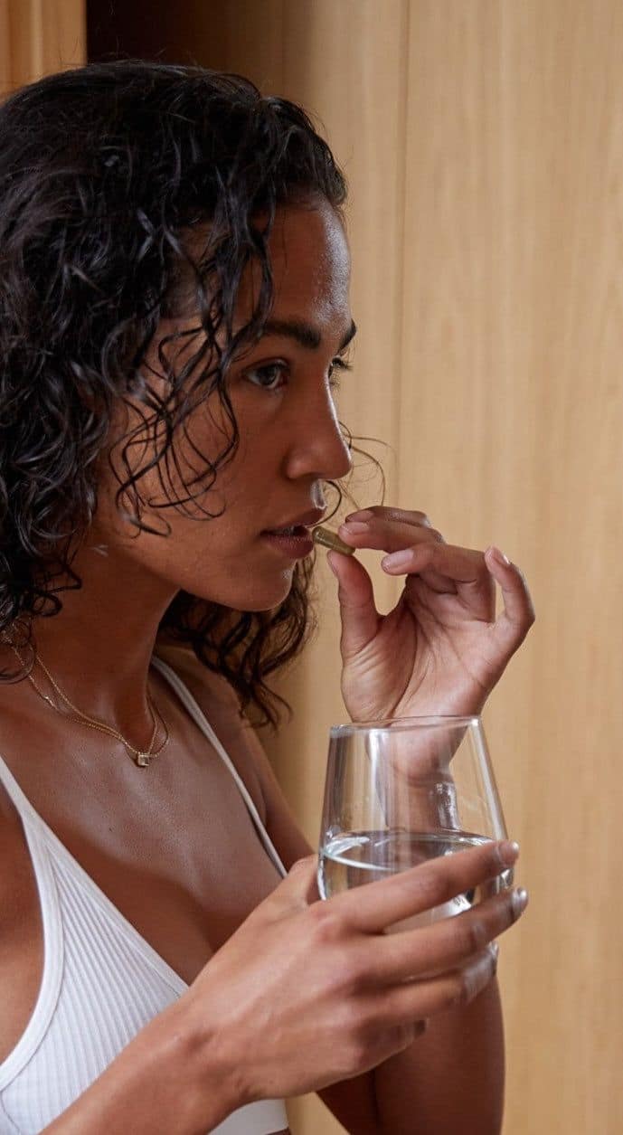 Mujer sosteniendo cápsulas de suplemento de magnesio con un vaso de agua, representando el uso responsable de suplementos
